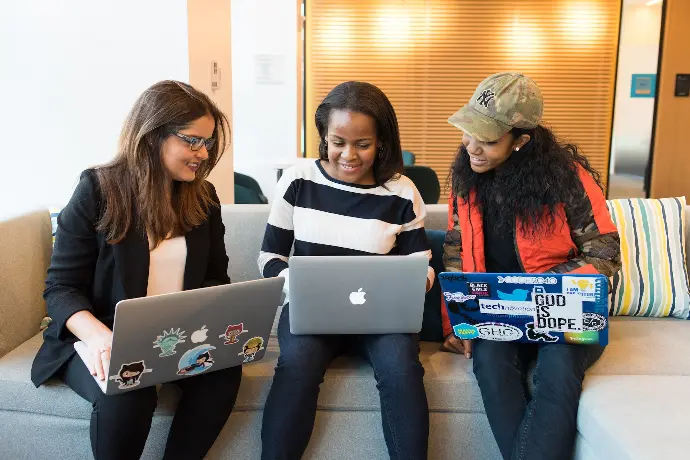 tres mujeres sentadas en un sofá con un MacBook