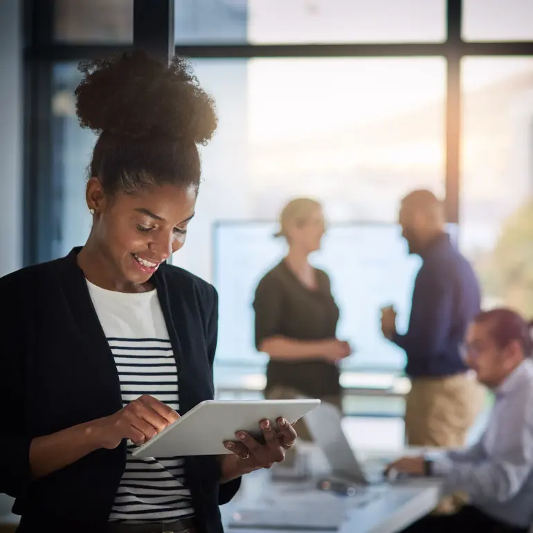 Woman working with a tablet with officemates behind her